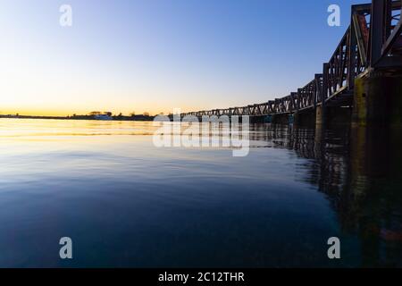 Les lignes épurées du pont ferroviaire historique de Tauranga, avec le soleil levant à gauche, ont jeté des teintes dorées à travers l'horizon du port, en Nouvelle-Zélande. Banque D'Images