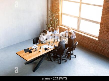 Collègues multiraciaux tenant les mains assis à une table au bureau Banque D'Images