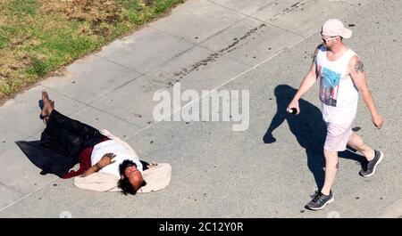 Venise, Californie, États-Unis. 13 juin 2020. Comme un homme sans abri dort sur la promenade de Venice Beach, les passants l'ignorent pour la plupart. Dans l'heure environ que cet homme a été photographié, peu de gens se sont arrêtés pour vérifier son bien-être. Dans deux cas, les hommes ont sauté sur lui comme s'ils étaient en compétition dans le sport du ''bum jumping'. À la fin de l'heure, un camion du service des incendies de Los Angeles s'est tiré sur les lieux et l'homme a été convaincu de se déplacer sur l'herbe adjacente. Crédit : Brian Cahn/ZUMA Wire/Alay Live News Banque D'Images