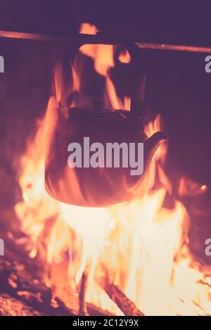 La bouilloire est chauffée sur un feu lumineux la nuit en extérieur, photo tonifiée Banque D'Images