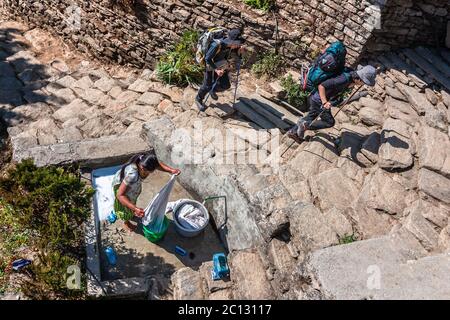 Pokhara, Népal - janvier 2011 : femme lavant des vêtements et randonneurs dans un village de montagne Banque D'Images