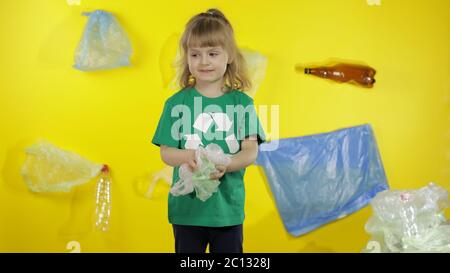 Jeune activiste bénévole dans un t-shirt avec logo de recyclage. Collecte les emballages en cellophane du sol. Arrière-plan avec sacs, bouteilles. Sauver l'environnement terrestre. Pollution par nature des déchets plastiques Banque D'Images