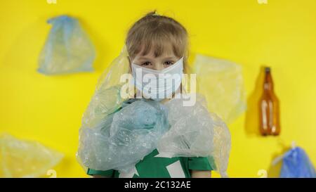 Triste activiste fille dans t-shirt avec le logo de recyclage dans des emballages en plastique sur son cou et la tête. Fond avec sacs de cellophane, flacons. Réduire la pollution par les déchets de plastique. Protection de l'environnement écologique Banque D'Images