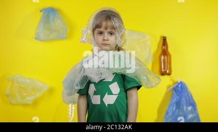 Triste activiste fille dans t-shirt avec le logo de recyclage dans des emballages en plastique sur son cou et la tête. Fond avec sacs de cellophane, flacons. Réduire la pollution par les déchets de plastique. Pensez vert. Sauver l'environnement écologique Banque D'Images