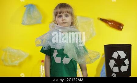 Triste activiste fille dans t-shirt avec le logo de recyclage dans des emballages en plastique sur son cou et la tête. Fond avec sacs de cellophane, flacons. Réduire la pollution par les déchets de plastique. Pensez vert. Sauver l'environnement écologique Banque D'Images