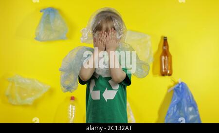 Triste activiste fille dans t-shirt avec le logo de recyclage dans des emballages en plastique sur son cou et la tête. Fond avec sacs de cellophane, flacons. Réduire la pollution par les déchets de plastique. Pensez vert. Sauver l'environnement écologique Banque D'Images