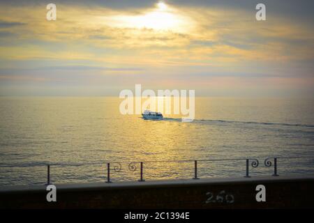 Un petit bateau solitaire fait une croisière sur la mer Ligurienne sous un ciel coloré et se rapproche du coucher du soleil sur la côte des Cinque Terre, en Italie Banque D'Images