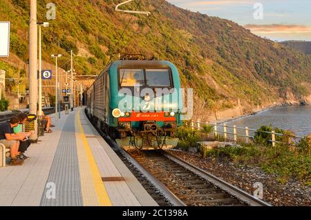 Un train se déplace dans l'Monterosso al Mare gare sur la côte des Cinque Terre de l'Italie en tant que voyageurs s'asseoir et profiter d'une journée chaude au début de l'automne Banque D'Images