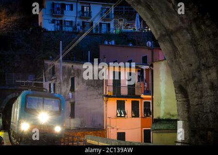 Un train de nuit les phares de briller alors qu'il entre dans un tunnel dans la soirée à Vernazza Italie, sur la côte des Cinque Terre avec la colline derrière la ville Banque D'Images