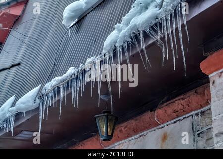 Des glaçons à pointes au bord d'un toit gris incliné avec des amas de neige en hiver Banque D'Images