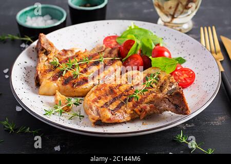 Steaks de porc grillés et salade avec tomates sur fond sombre. Banque D'Images