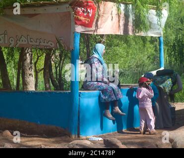 Une marocaine avec foulard attend avec ses enfants dans une cabine vide sur le côté de la route près de Marrakech au Maroc Banque D'Images