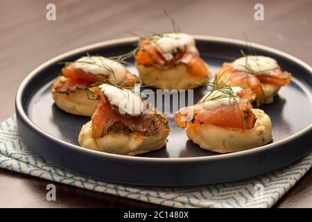 gravlax de saumon fumé séché avec aneth et crème sure sur pancake blini et plaque en céramique bleue et serviette sur table en bois Banque D'Images