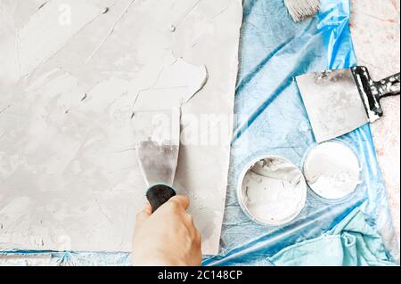 Spatule métallique à la main met du mastic sur la surface de la planche, un pot de ciment, un pinceau pour peinture molaire, un chiffon bleu et un revêtement de sol en cellophane bleu. Self-r Banque D'Images