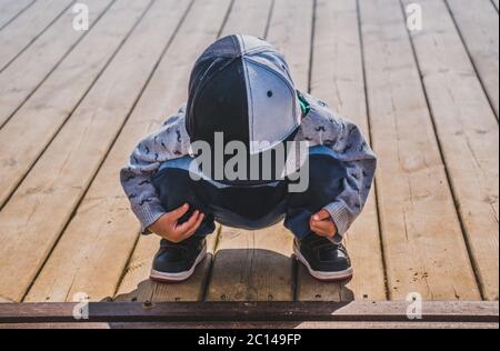 Petit garçon en casquette de baseball assis en position de squat sur une surface plantée en bois Banque D'Images