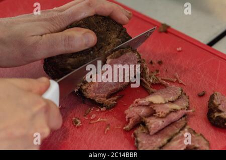 couper à la main des tranches de pastrami sur la planche à découper pour préparer une recette Banque D'Images