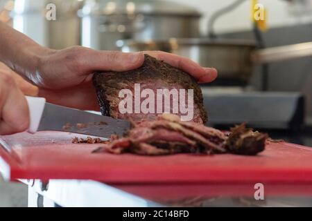 couper à la main des tranches de pastrami sur la planche à découper pour préparer une recette Banque D'Images