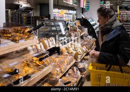 Femme avec des supports de veste dans le supermarché aux étagères avec du pain et des pâtisseries. Concentrez-vous sur les sacs de papier avec du pain au centre de la photo Banque D'Images