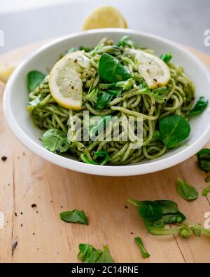 Pâtes végétaliennes avec sauce trempée à l'avocat, feuilles d'épinards et citron dans un bol blanc. Sur fond en bois. Des aliments sains végétariens Banque D'Images