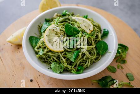 Pâtes végétaliennes avec sauce trempée à l'avocat, feuilles d'épinards et citron dans un bol blanc. Sur fond en bois. Des aliments sains végétariens Banque D'Images