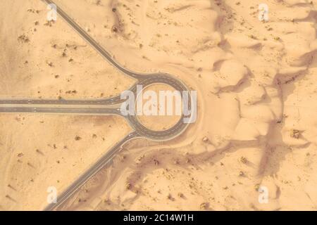 Vue aérienne d'une route et d'un rond-point de passage au milieu d'un désert sablonneux à la lumière de l'après-midi. Banque D'Images