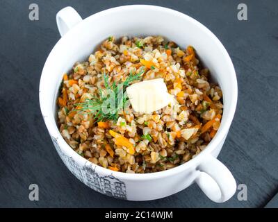 Porridge avec légumes dans un bol blanc. Garni d'une branche de persil. Sarrasin avec oignons et carottes. Banque D'Images