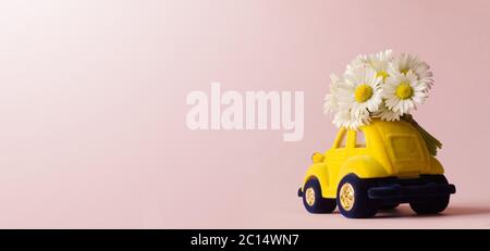 Carte avec une petite voiture de jouet livrant blanc bouquet de fleurs sur fond rose. Banque D'Images