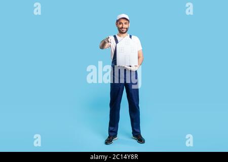 Homme de main plein sourire en uniforme tenant la maison de papier et pointant vers l'appareil photo. Un homme de la motionnaire offrant de l'aide dans la relocalisation, les services de réparation à domicile et ma Banque D'Images