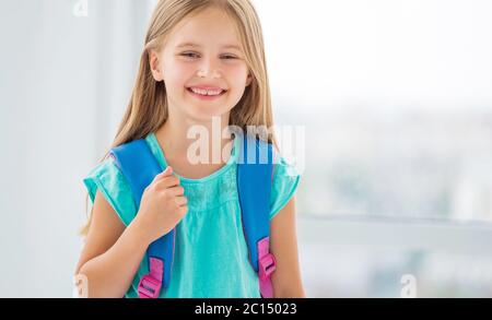 Magnifique fille souriante écolière en chemise bleue avec nouveau sac à dos est prête à aller à l'école Banque D'Images