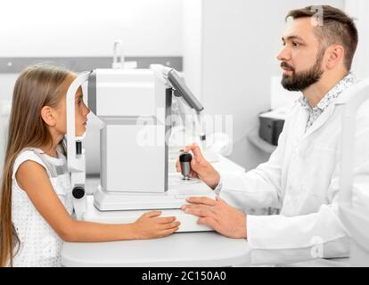 ophtalmologiste tenant l'équipement d'oeil examinant les yeux de la fille dans la clinique Banque D'Images