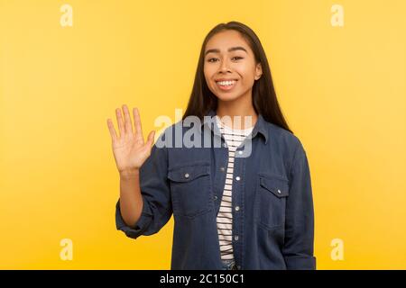 Bonjour, bienvenue ! Portrait de sympathique fille heureuse en chemise en denim agitant la main en signe de bonjour ou au revoir, salutation avec le sourire, expression amicale et accueillante Banque D'Images