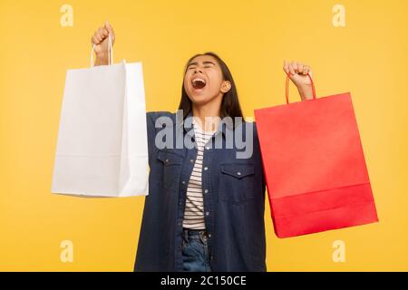 Portrait de la cashopper girl surjoyée dans un élégant maillot en denim levant des sacs et criant du bonheur, émerveillé par les achats dans le magasin de mode, thri Banque D'Images