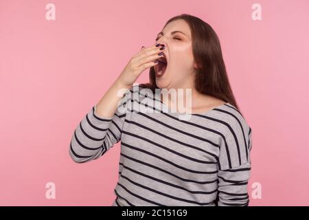 Insomnie. Portrait d'une femme endormie fatiguée dans un sweat-shirt rayé bâchant et couvrant la bouche avec la main, se sentant somnolent après une nuit sans sommeil Banque D'Images