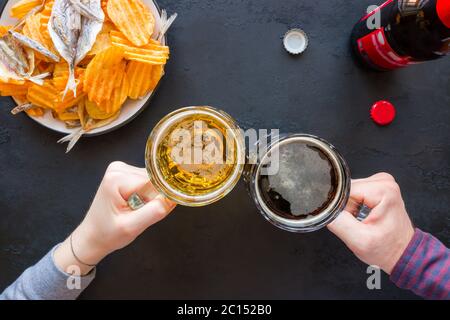 Les gens gardent des mugs avec de la bière sombre et légère sur le fond des collations de frites et de poisson Banque D'Images