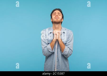 Je vous prie ! Portrait de l'homme frustré dans le maillot en denim gardant les mains dans le geste de prière, appelant à dieu avec l'expression implacable, sincère comme Banque D'Images