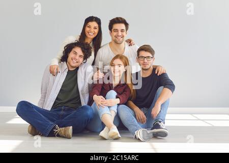 Un groupe d'amis est assis à l'étage dans une chambre sur un fond gris. Banque D'Images