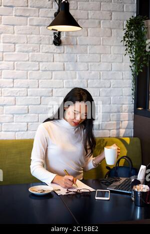 Femme asiatique travaillant sur un ordinateur portable et prenant un café dans un bar. Travail à distance en ligne hors du bureau Banque D'Images