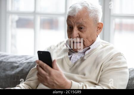 Gros plan surpris, un homme mûr et enthousiaste regardant l'écran du téléphone Banque D'Images