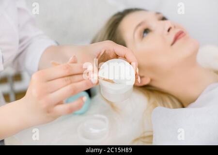 Image rognée en gros plan des mains d'une femme médecin cosmetologue tenant un pot de crème et une spatule en bois dans ses mains. Jolie jeune femme couché sur le Banque D'Images