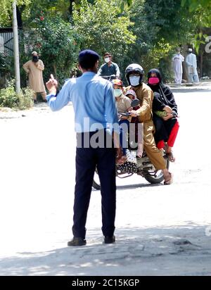 Islamabad, Pakistan. 14 juin 2020. Un policier arrête une famille sur une moto qui pénètre dans une zone résidentielle fermée à l'air libre après que certaines personnes ont testé positif pour le COVID-19 à Islamabad, capitale du Pakistan, le 14 juin 2020. Le gouvernement pakistanais a commencé à assouplir le verrouillage de la COVID-19 à partir de mai et a adopté une stratégie appelée verrouillage intelligent pour ne fermer que les zones où des cas confirmés de COVID-19 sont signalés afin de freiner la propagation de la maladie. Crédit : Ahmad Kamal/Xinhua/Alamy Live News Banque D'Images