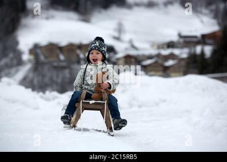 Mignon garçon jouant avec l'ours en peluche dans la neige, en hiver. Un petit tout-petit jouant avec des jouets par temps de neige Banque D'Images