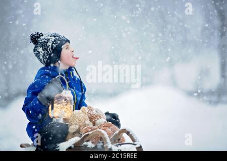 Mignon garçon jouant avec l'ours en peluche dans la neige, en hiver. Un petit tout-petit jouant avec des jouets par temps de neige Banque D'Images