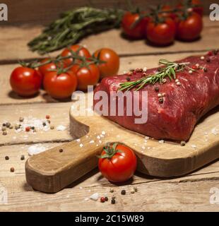 Steak de bœuf cru sur une planche à découper avec du romarin et des épices. Banque D'Images