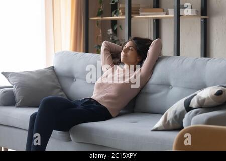 Jeune femme détendue et satisfaite, reposant sur un canapé confortable à la maison