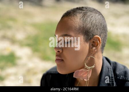 Gros plan de la petite fille noire calme avec boucles d'oreilles en plumes écoutant les sons de la nature avec les yeux fermés Banque D'Images