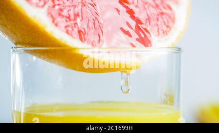 Image macro de la goutte de jus accrochée sur le pamplemousse mûr frais et tombant dans le verre Banque D'Images