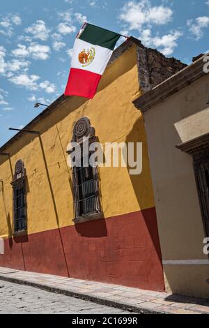 Le drapeau mexicain flotte contre un ciel bleu et un bâtiment colonial classique le long de la Calle Quebrada dans le quartier historique de San Miguel de Allende, Mexique. Banque D'Images