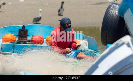 Palmar, Santa Elena / Equateur - octobre 19 2019: Pêcheur artisanal couture son filet sur son bateau au bord de la rivière avec des oiseaux en arrière-plan Banque D'Images