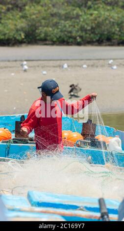 Palmar, Santa Elena / Equateur - octobre 19 2019: Pêcheur artisanal couture son filet sur son bateau au bord de la rivière avec des oiseaux en arrière-plan Banque D'Images