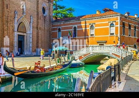 Venise, Italie, 13 septembre 2019 : gondoles et bateaux amarrés sur un canal d'eau étroit, basilique Santa Maria Gloriosa dei Frari Eglise catholique et pont en pierre, région de Vénétie, ciel bleu en été Banque D'Images